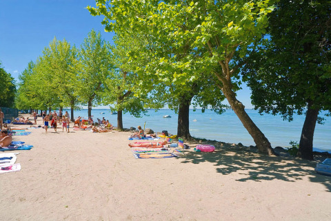 Playa con bañistas, árboles y toallas en Camping Cisano/San Vito, parque vacacional en Véneto, Italia.