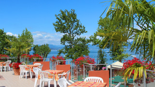 Terrace overlooking the lake at Camping Cisano/San Vito, Veneto, Italy, with tables and palm trees.