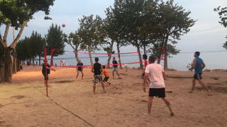Holiday park guests play volleyball on a sandy beach with trees and lake view at Camping Cisano/San Vito.