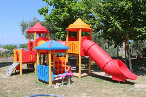 Parco giochi con struttura colorata e scivolo sotto gli alberi al Camping Cisano/San Vito, Veneto, Italia.