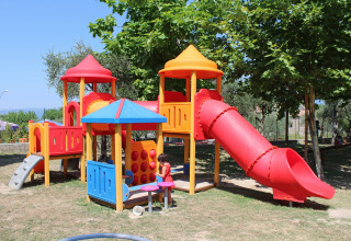 Parco giochi con struttura colorata e scivolo sotto gli alberi al Camping Cisano/San Vito, Veneto, Italia.