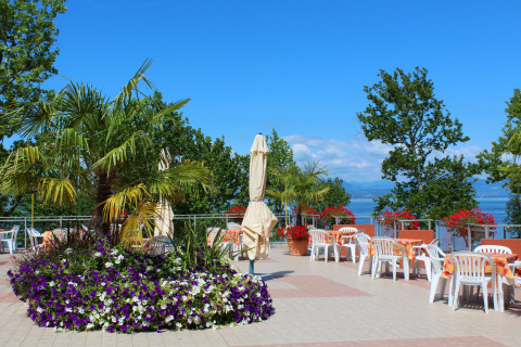 Terrazza all'aperto al Camping Cisano/San Vito in Veneto, Italia, con sedie, tavoli e vista lago.