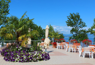 Terrasse extérieure du Camping Cisano/San Vito en Vénétie, Italie, avec chaises, tables et vue sur le lac.