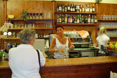 Een vrouw helpt een klant aan de bar met flessen en glazen op Camping Cisano/San Vito, Italië.