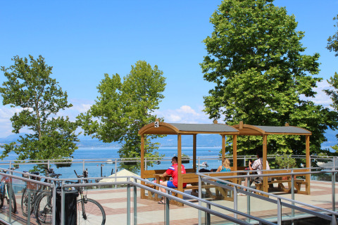 Huéspedes descansan bajo pérgolas de madera con vistas al lago en Camping Cisano/San Vito, Véneto, Italia.