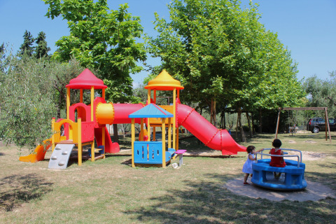 Colorido parque infantil con toboganes y niños jugando, rodeado de árboles en Camping Cisano/San Vito, Veneto, Italia.
