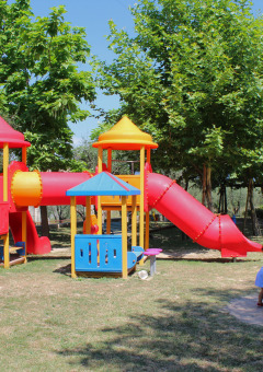 Colorful playground with slides and children playing, surrounded by trees at Camping Cisano/San Vito in Veneto, Italy.