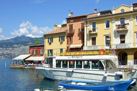 Colorful lakeside houses and passenger boat with mountain view in Cisano di Bardolino, Veneto, Italy.