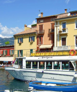 Colorful lakeside houses and passenger boat with mountain view in Cisano di Bardolino, Veneto, Italy.