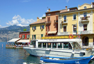 Gekleurde huizen en een rondvaartboot bij het water in Cisano di Bardolino, Veneto, Italië, met bergen.