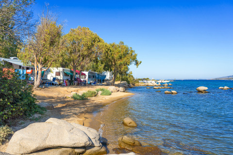 Caravanas y tiendas entre árboles en la playa de Camping Gasparina, Véneto, Italia, con vistas al mar.