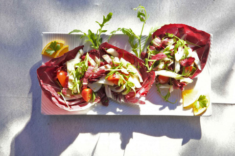 Colorful salad in radicchio leaves with tomatoes and lemon on a white plate, Camping Gasparina, Veneto, Italy.
