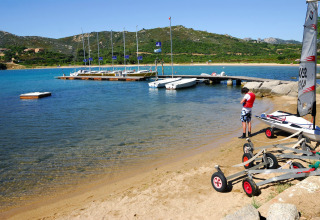 Persona sulla spiaggia vicino a un pontile e barche a vela al Camping Gasparina, villaggio in Veneto, Italia.