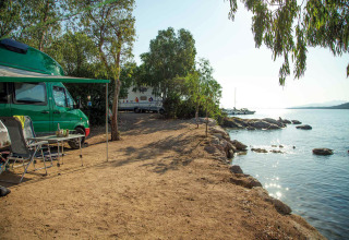 Campsite by the lake with motorhome, chairs, and trees at Camping Gasparina holiday park in Veneto, Italy.