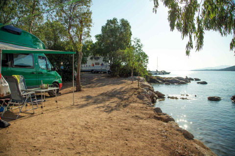 Zona de camping junto al lago con autocaravana, sillas y árboles en Camping Gasparina, Veneto, Italia.