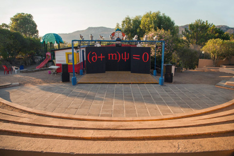 Palco all'aperto al Camping Gasparina, Veneto, Italia, con un'equazione matematica e un parco giochi sullo sfondo.