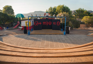 Outdoor stage at Camping Gasparina, Veneto, Italy, featuring a mathematical equation and a playground behind.