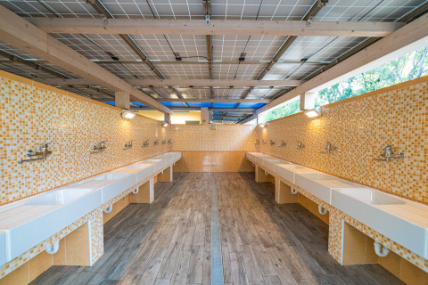 Zona de fregaderos compartida con azulejos de mosaico amarillos en Camping Gasparina, Véneto, Italia.