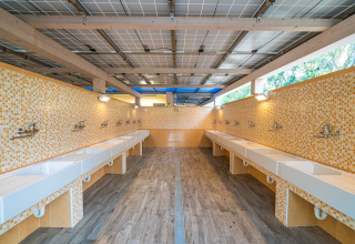 Zona de fregaderos compartida con azulejos de mosaico amarillos en Camping Gasparina, Véneto, Italia.