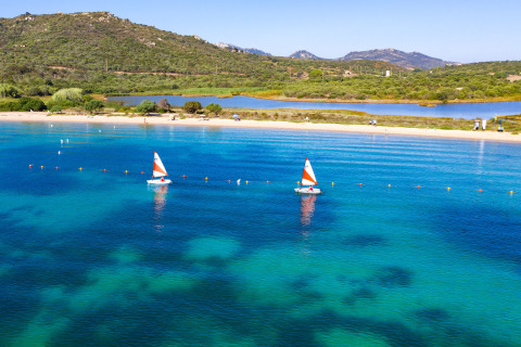 Dos veleros pequeños con velas naranjas navegan en aguas azules junto a la playa de Camping Gasparina, Véneto.