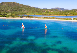 Two small sailboats with orange sails on clear blue water near the beach at Camping Gasparina, Veneto, Italy.