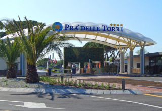 Ingresso del Camping Pra'delle Torri a Veneto, Italia, con palme e una struttura moderna e accogliente.