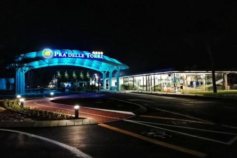 Entrada al Camping Pra’delle Torri en Véneto, Italia, iluminada con luces azules durante la noche.