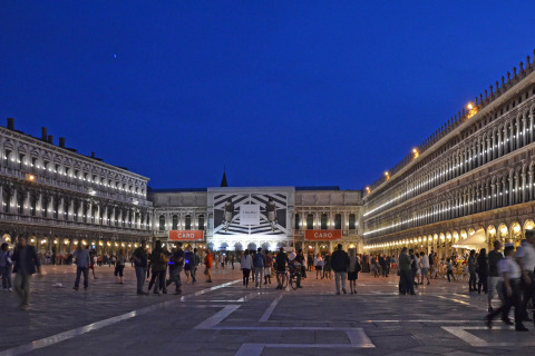A square in Venice, Veneto, Italy at night with people, illuminated historic buildings and clear blue sky.