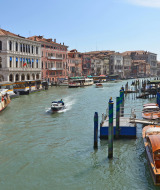 Animado canal en una ciudad italiana con botes, edificios históricos y gente paseando por la orilla.