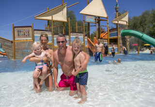 Familie nyder en solrig dag ved børnepoolen med piratskib i Camping Pra'delle Torri, Veneto, Italien.