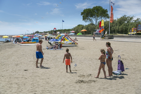 Camping Pra'delle Torri, Veneto, Italia: famiglia sulla spiaggia sabbiosa con ombrelloni e giochi d'acqua.