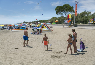 Camping Pra'delle Torri, Vénétie, Italie : famille sur la plage de sable avec parasols et activités nautiques.