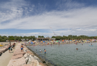 Strandscene ved Camping Pra'delle Torri i Veneto, Italien, med badegæster, parasoller og klart vand.