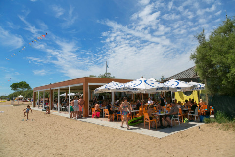 Zonnekloppers genieten bij een strandcafé met oranje stoelen op Camping Pra'delle Torri in Veneto, Italië.