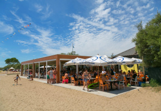Zonnekloppers genieten bij een strandcafé met oranje stoelen op Camping Pra'delle Torri in Veneto, Italië.