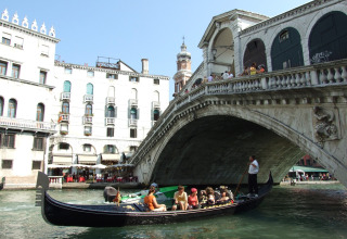 Gondola con turisti che passa sotto l’iconico Ponte di Rialto a Venezia, Italia, in una giornata di sole.