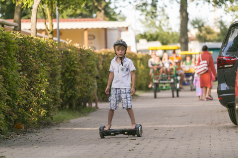 En dreng med hjelm kører på et hoverboard på en sti i Camping Pra'delle Torri, Veneto, Italien.