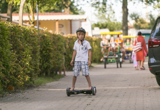 En dreng med hjelm kører på et hoverboard på en sti i Camping Pra'delle Torri, Veneto, Italien.