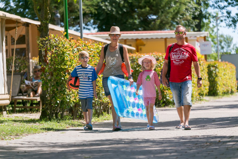 A family of four walks through Camping Pra'delle Torri holiday park in Veneto, Italy, dressed for swimming.