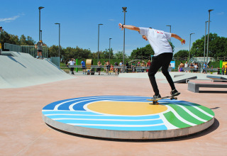 Skateboarder udfører et trick på en farverig cirkelrampe i skateparken på Camping Pra'delle Torri, Veneto.