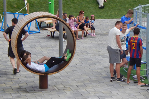Niños descansan en un columpio circular y personas conversan al aire libre en Camping Pra'delle Torri, Véneto, Italia.