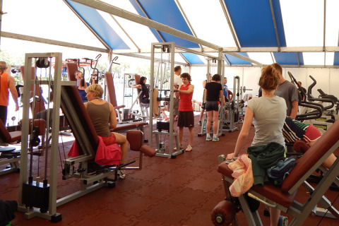 Gimnasio de parque vacacional en Italia, personas entrenando en máquinas bajo una carpa luminosa.