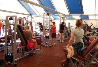 Ferieparkens fitnessrum fyldt med mennesker, der træner på motionsmaskiner i et lyst telt.