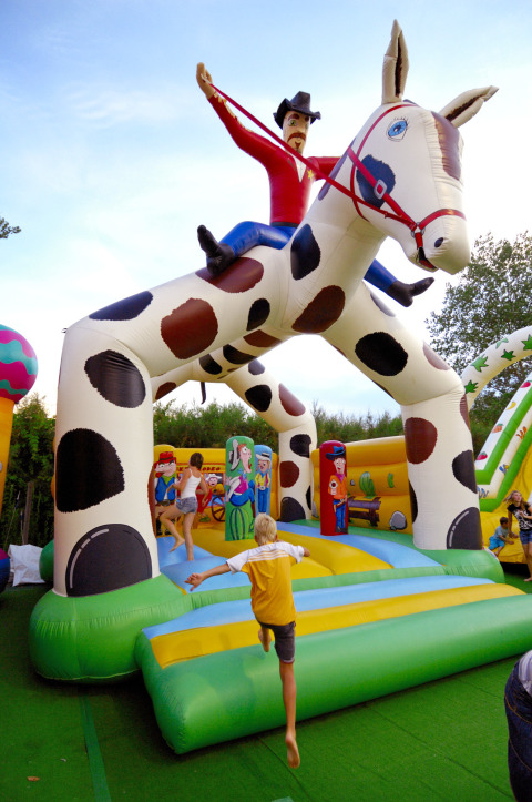 Bambini che giocano su un grande gonfiabile cowboy a cavallo al Camping Pra'delle Torri, Veneto, Italia.