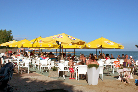 Outdoor beach café with yellow umbrellas at Camping Pra'delle Torri holiday park in Veneto, Italy, on a sunny day.