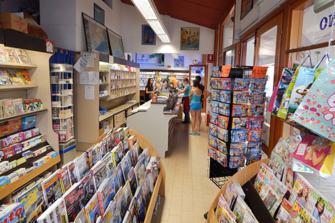 Interior de la tienda en Camping Pra'delle Torri, Véneto, Italia, con revistas y clientes en el mostrador.