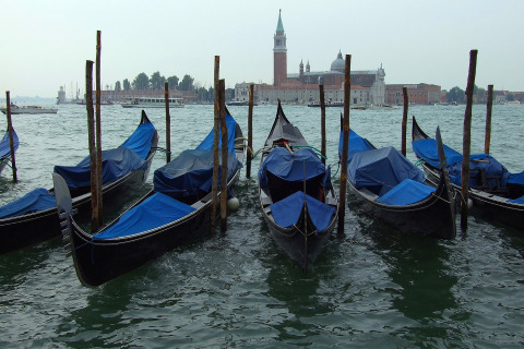 Góndolas atracadas en el agua con cubiertas azules y edificios históricos al fondo en Véneto, Italia.