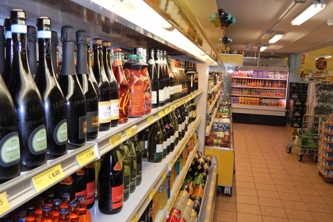Pasillo de supermercado en Camping Pra'delle Torri, Véneto, Italia, con botellas de vino y jugos en estantes.