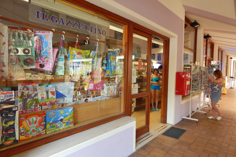 Escaparate con juguetes y revistas en Camping Pra'delle Torri, Veneto, Italia, con personas en el exterior.