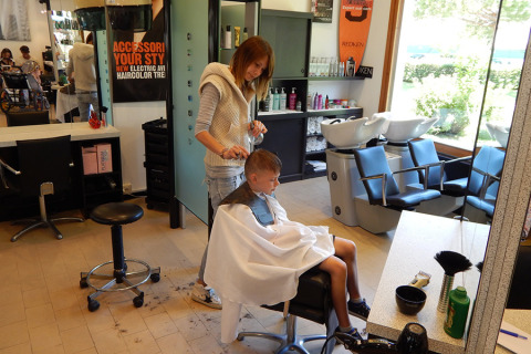 Een jongen krijgt een knipbeurt van een kapster in een moderne salon bij Camping Pra'delle Torri in Veneto, Italië.